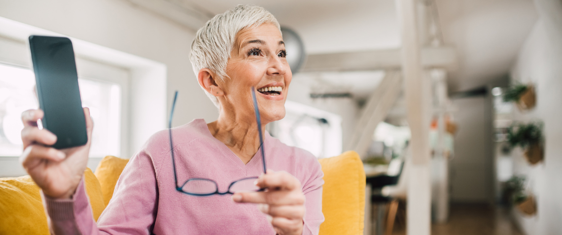 older-woman-happily-showing-her-smartphone-and-holding-her-glasses