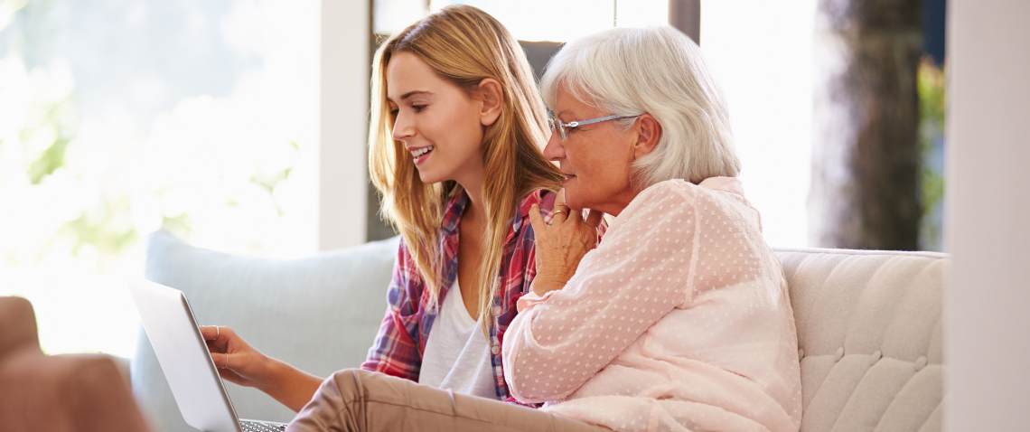 Middle-aged woman and senior woman sitting on a couch together looking at a laptop screen